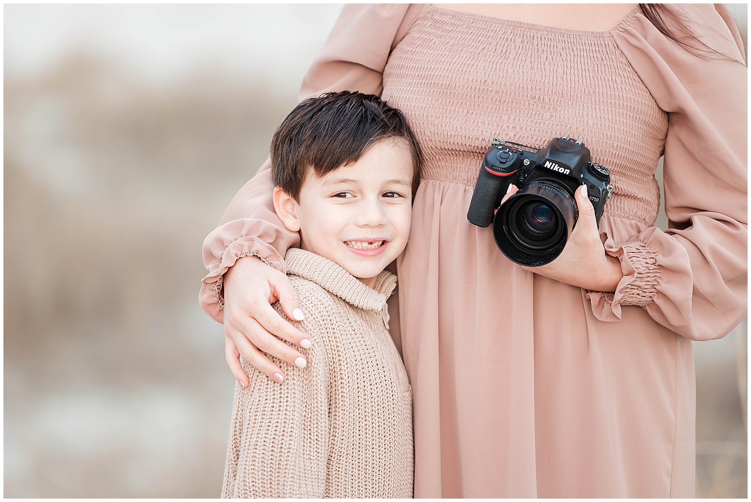 cute boy posing with mom and her camera on beach for photos.