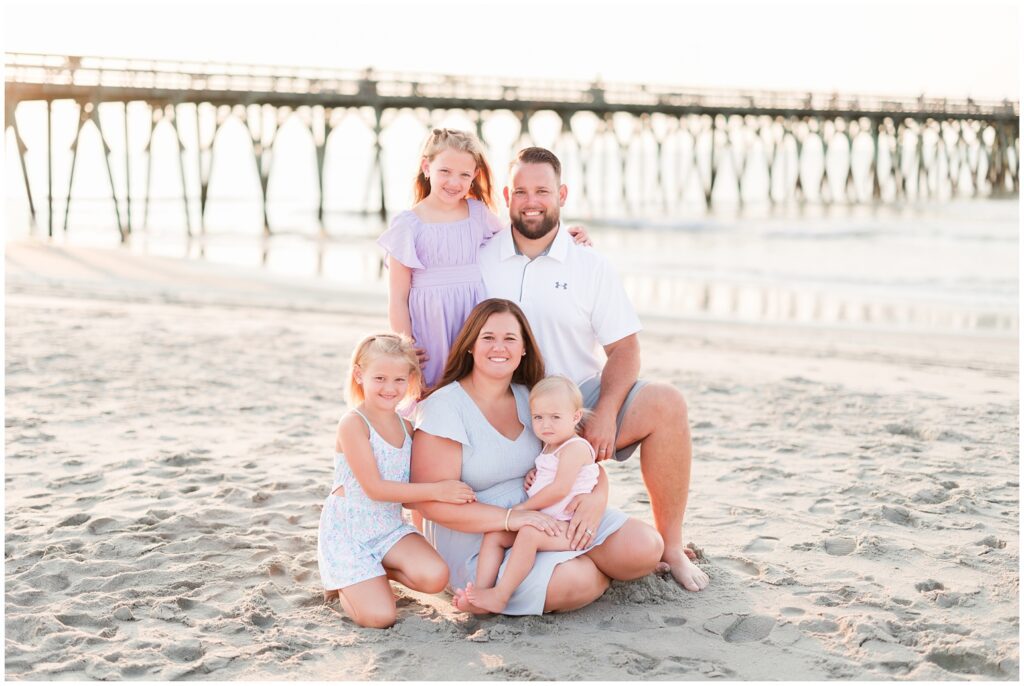 family of five sitting on the beach for their family photos