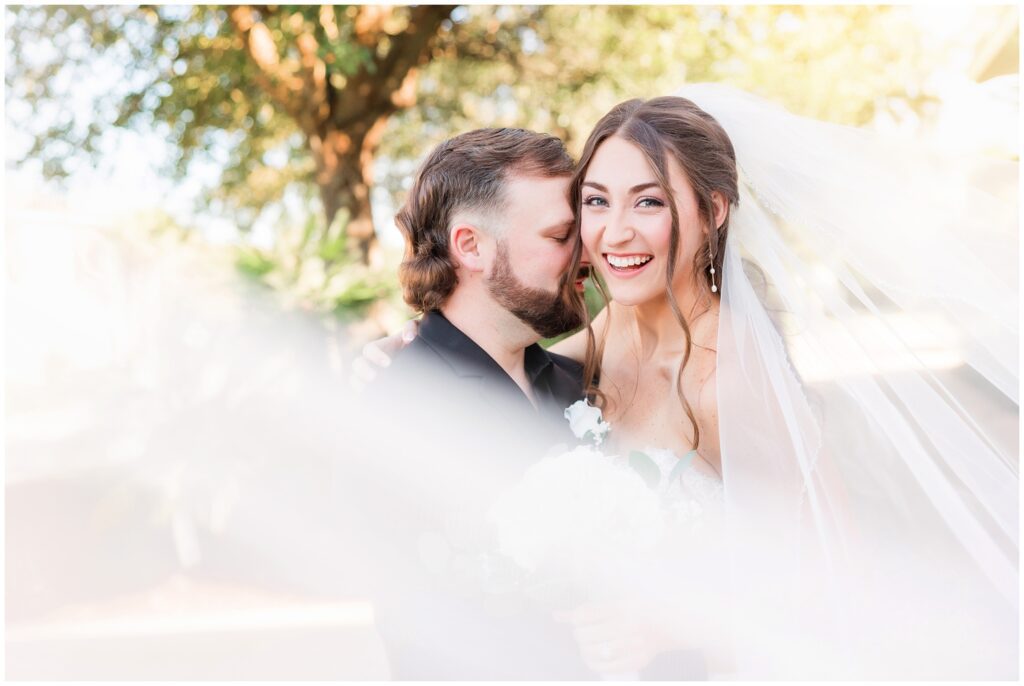 beautiful bride and groom posing for photos with photographer and veil 