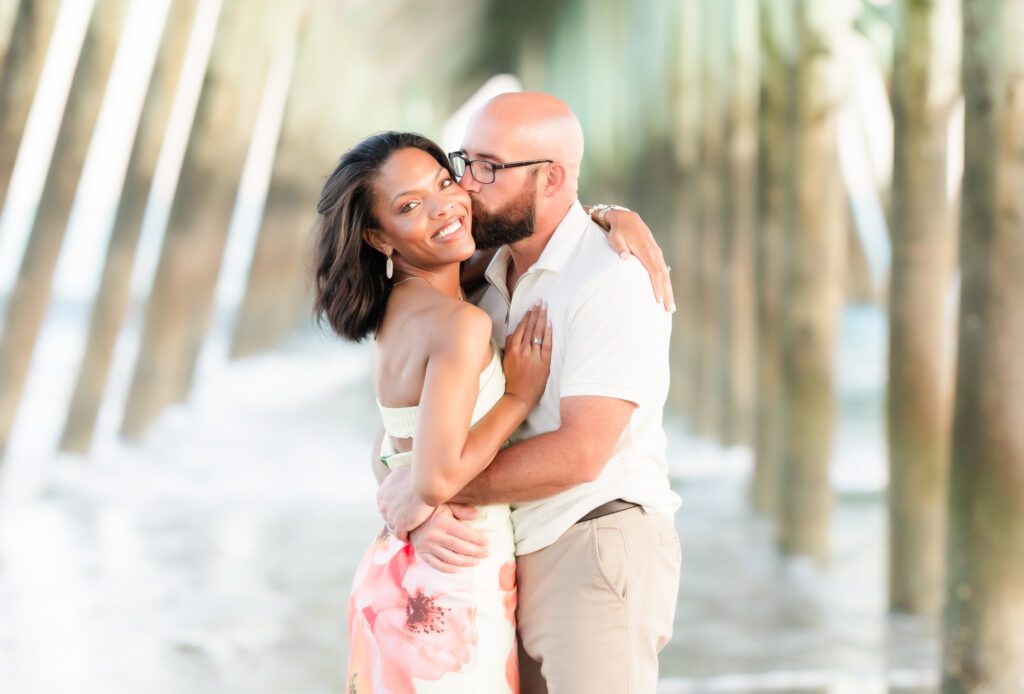 Couple laughing together on the beach under a pier. 